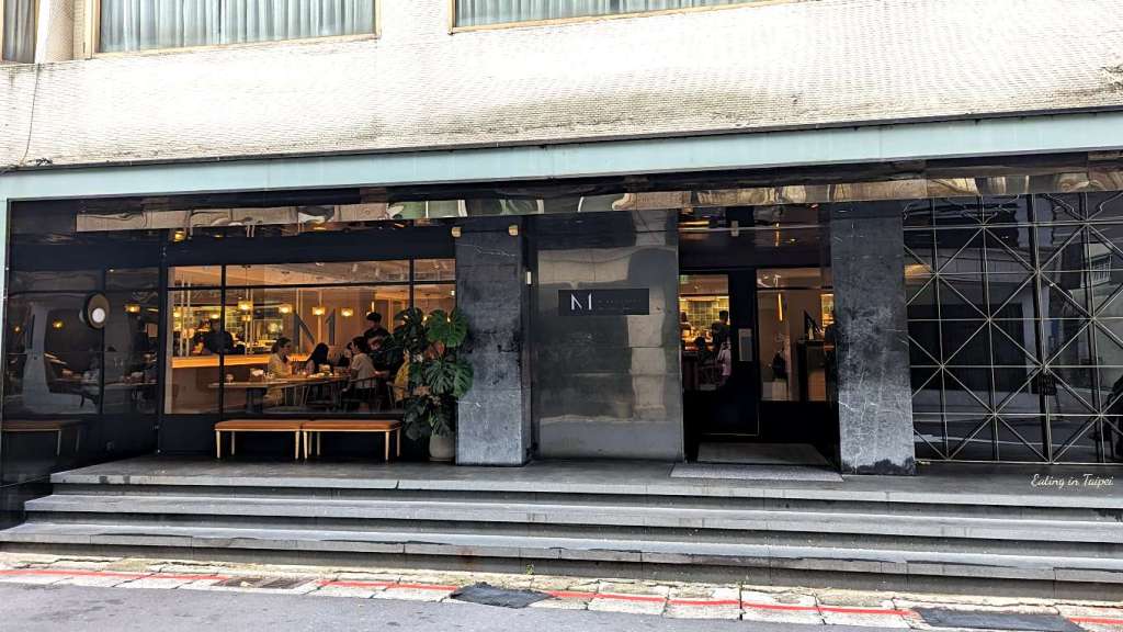 M One Cafe Daan from the outside - the space is set quite deep into the building it occupies, with darkness on the outside lit from the inside with warm light.